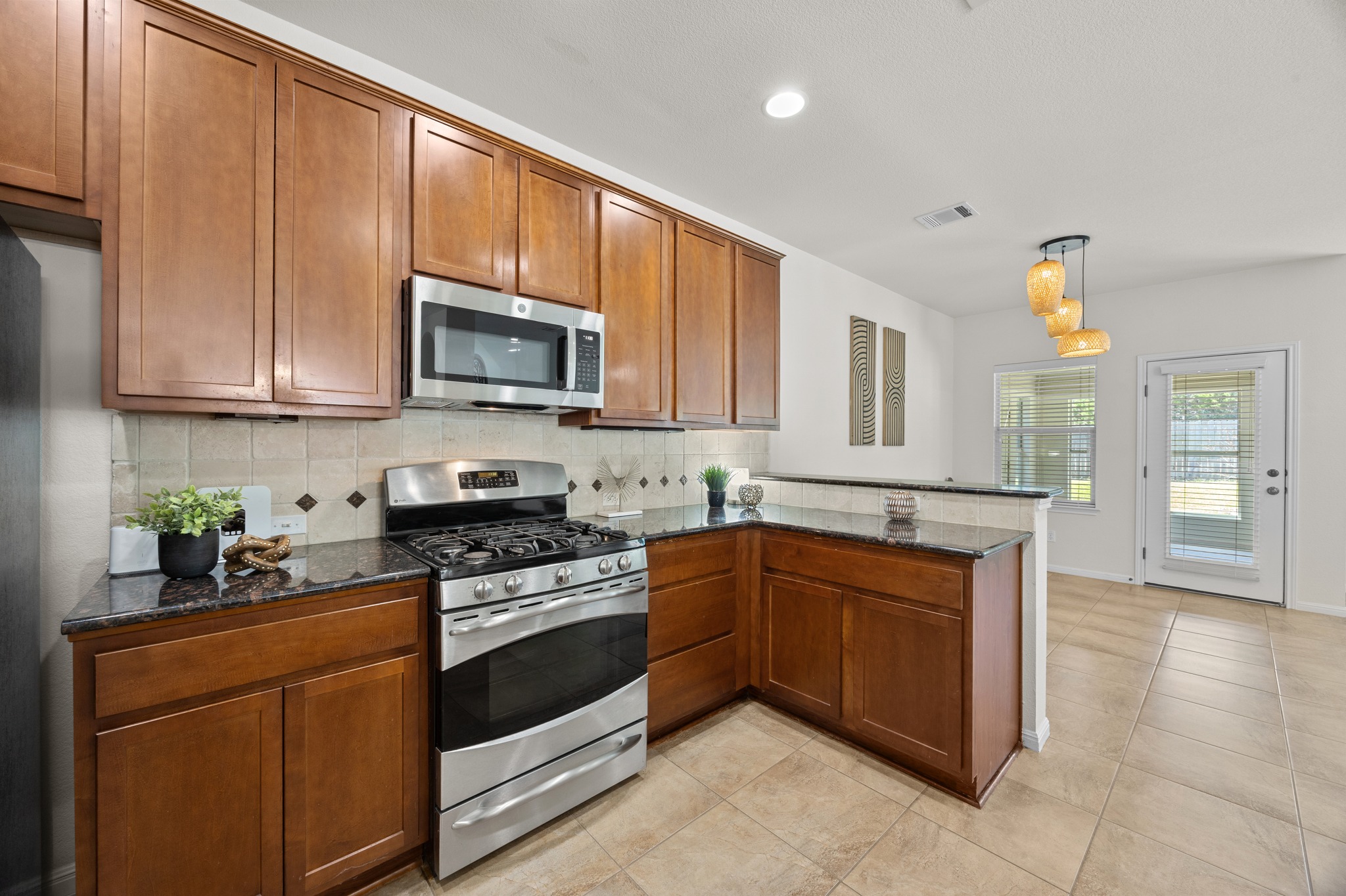 1317 Rimstone Drive Cedar Park, TX 78613 - Photo 17 of 32 Kitchen featuring stainless steel appliances, dark stone counters, wood finish cabinets, decorative backsplash, and a peninsula