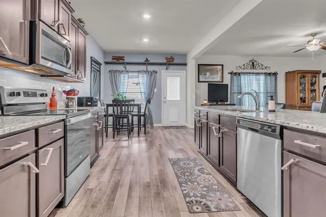 a kitchen with stainless steel appliances granite countertop a stove top oven a sink dishwasher a dining table and chairs with wooden floor