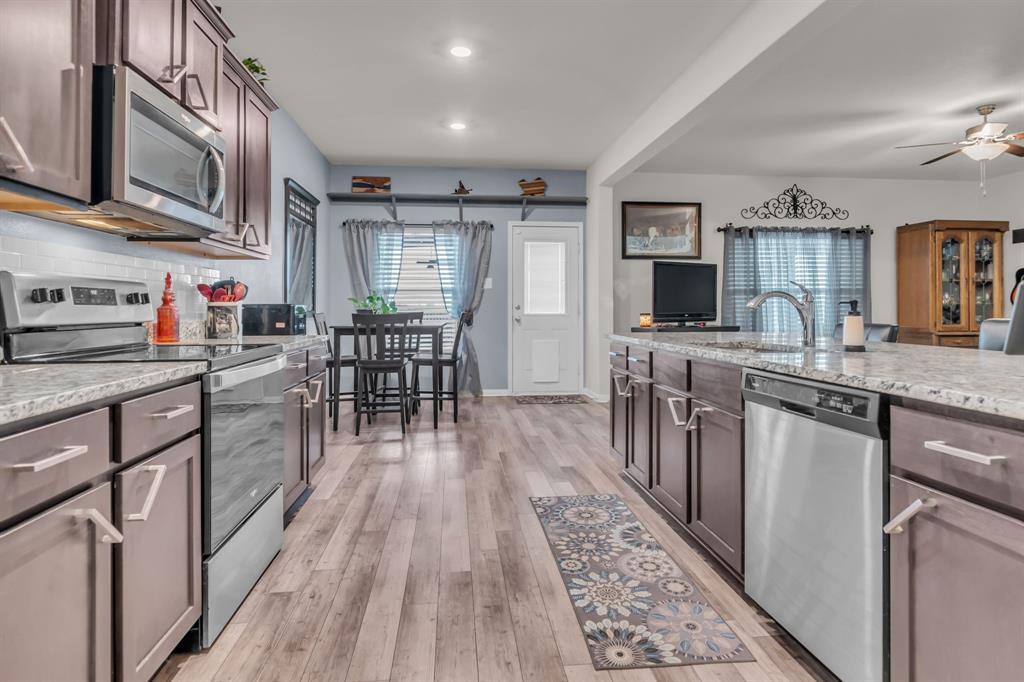 189 Point Rider Road Newark, TX 76071 - Photo 15 of 40 a kitchen with stainless steel appliances granite countertop a stove top oven a sink dishwasher a dining table and chairs with wooden floor