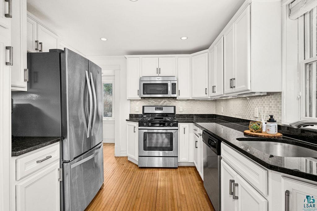 3206 Minnesota Avenue Duluth, MN 55802 - Photo 12 of 51 Kitchen featuring white cabinetry, stainless steel appliances, dark granite countertops, a mosaic tile backsplash, and wood-finish flooring