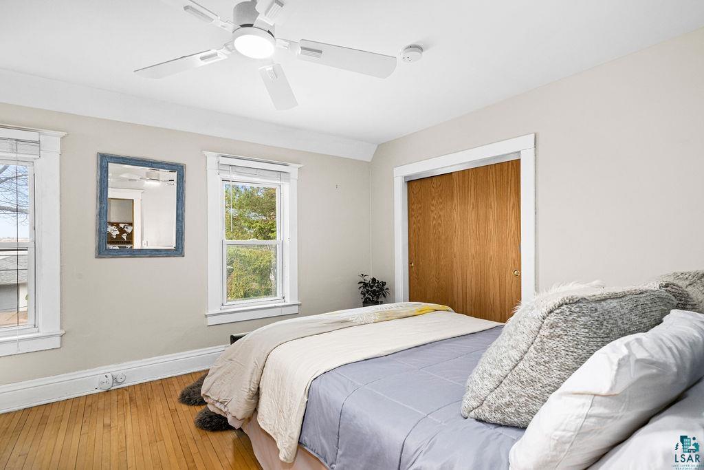 3206 Minnesota Avenue Duluth, MN 55802 - Photo 16 of 51 Master Bedroom featuring wood-finish flooring, two large windows with white trim, a ceiling fan with integrated lighting, and a two closets with master bath.