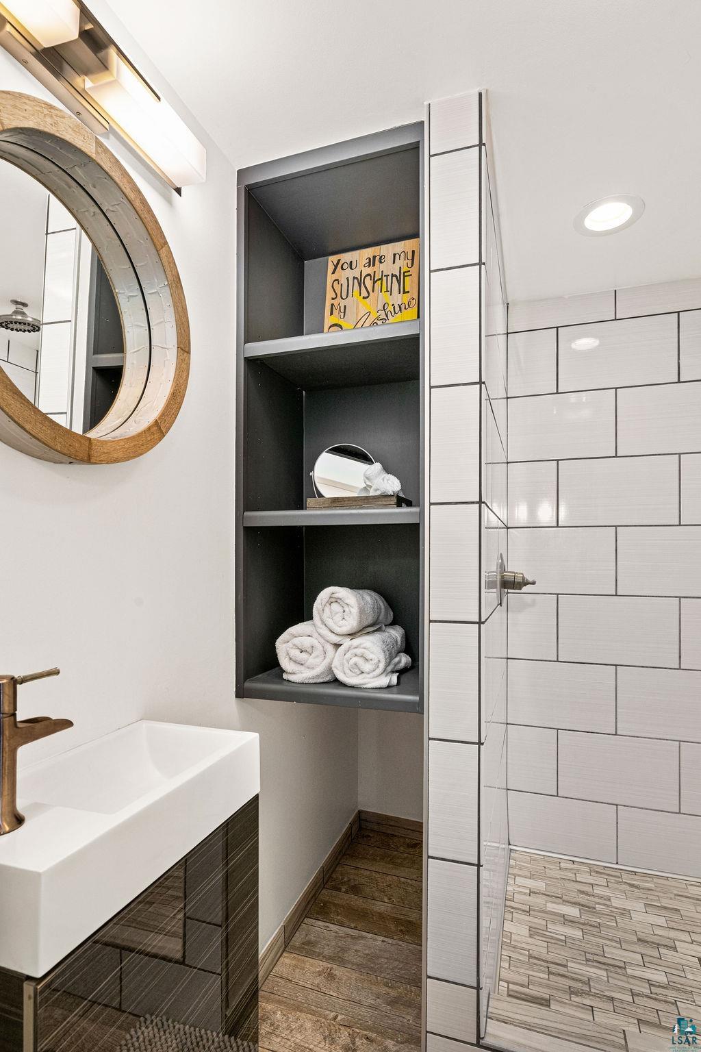 3206 Minnesota Avenue Duluth, MN 55802 - Photo 20 of 51 Bathroom featuring a floating vanity with a vessel sink and silver-finish faucet, built-in shelving, white subway tile shower surround, and wood-finish flooring