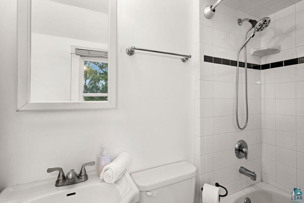 3206 Minnesota Avenue Duluth, MN 55802 - Photo 26 of 51 Bathroom featuring white tile walls with a black accent stripe, a tub/shower combination with a handheld shower head, and a white framed mirror