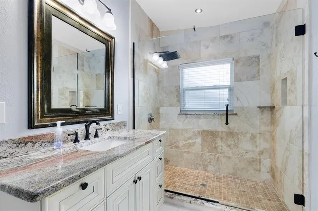 a bathroom with a granite countertop sink a mirror and shower