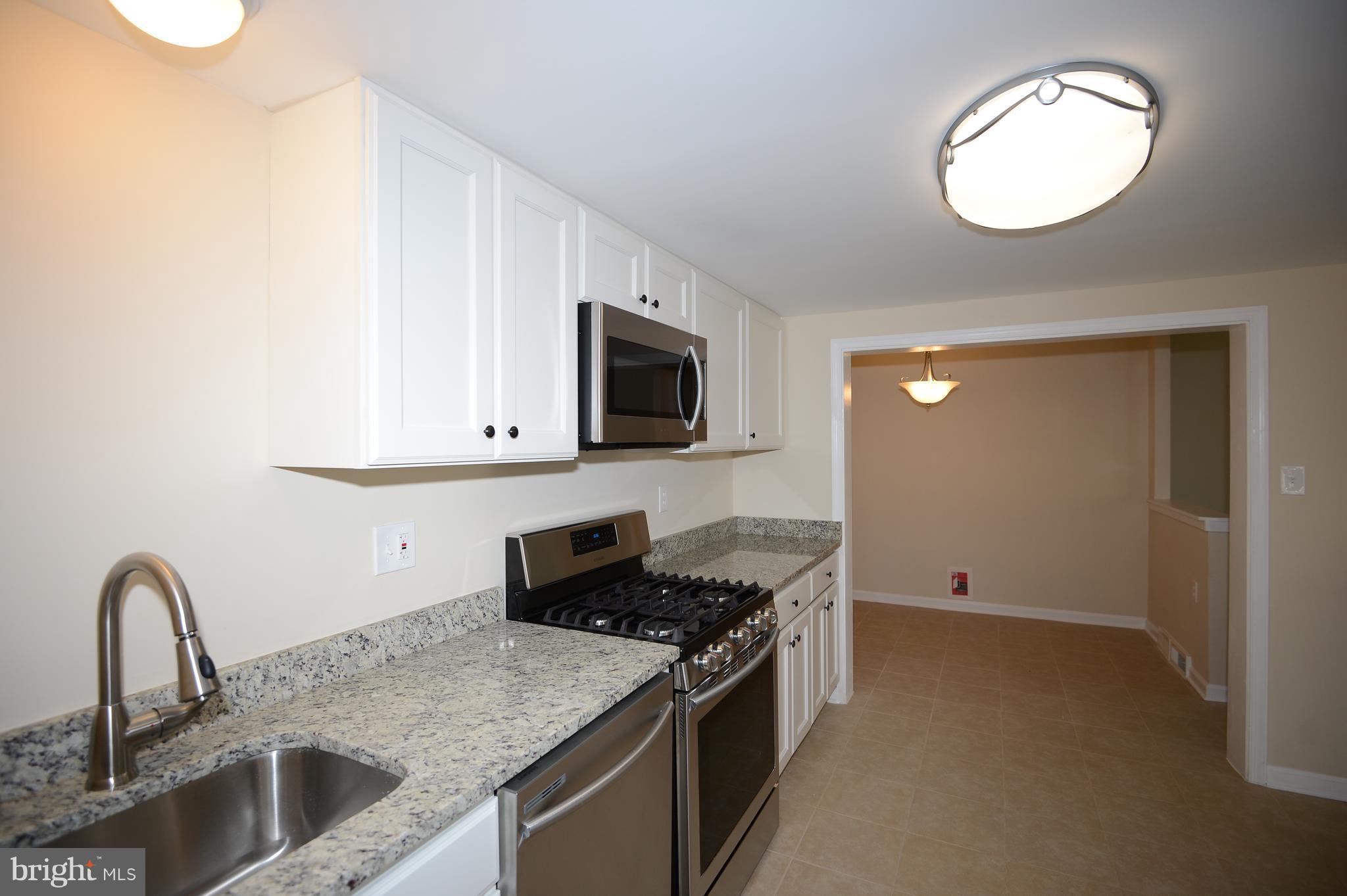 7500 Greenleaf Road Landover, MD 20785 - Photo 10 of 22 a kitchen with granite countertop a sink and a stove top oven with wooden floor