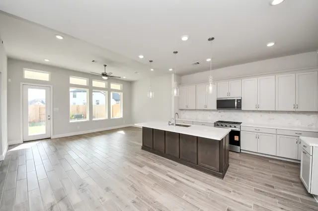 a large white kitchen with kitchen island a sink wooden floor and a refrigerator