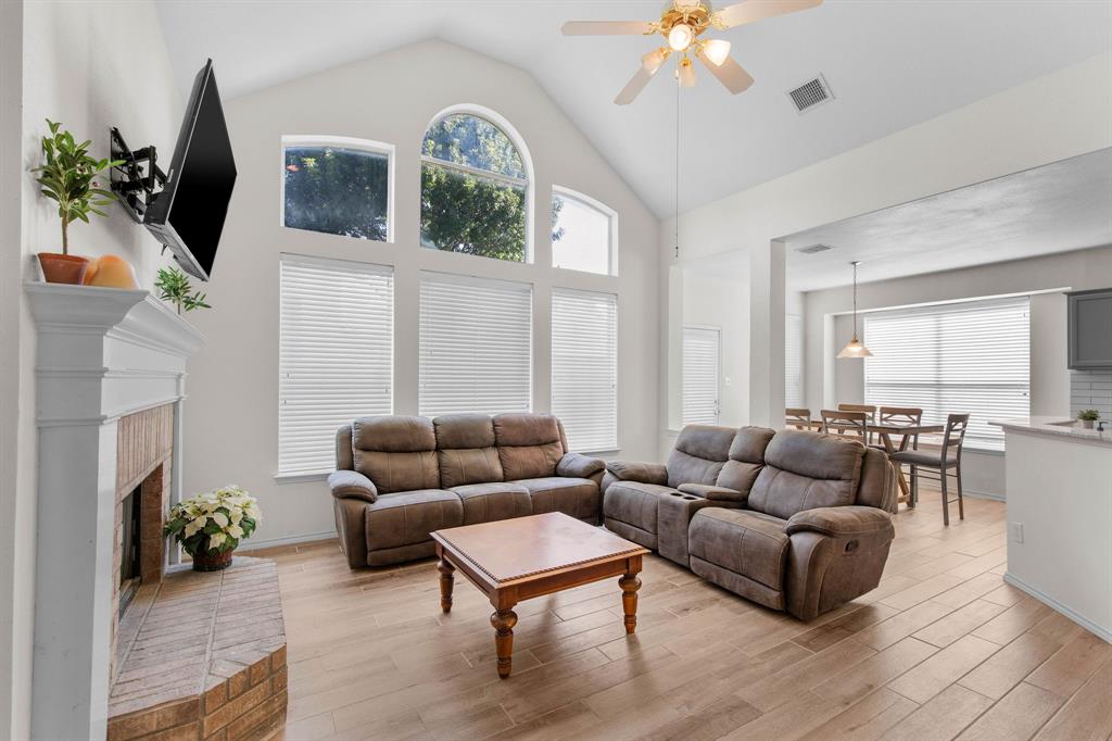 2700 Hereford Road Denton, TX 76210 - Photo 8 of 36 Vaulted ceilings with a ceiling fan, abundant natural light from multiple windows, wood-finish flooring, a brick fireplace with a white mantel, and an open layout to an adjoining dining area
