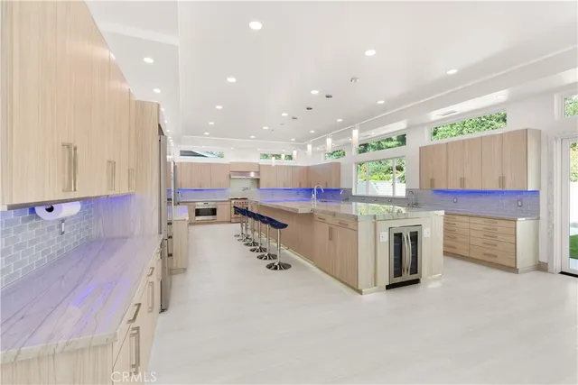 a large kitchen with stainless steel appliances kitchen island a large counter top a stove a chimney a sink and a refrigerator