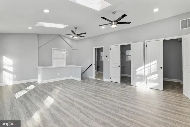 a view of an empty room with wooden floor and a ceiling fan