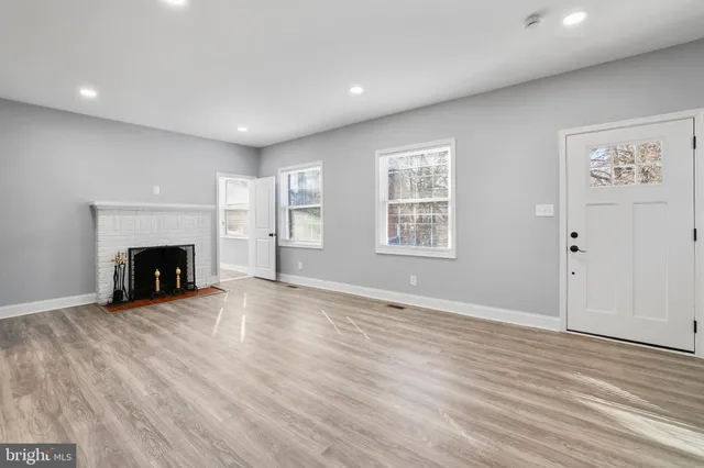 a view of an empty room with wooden floor fireplace and a window