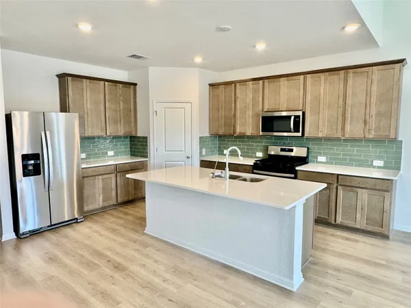 a kitchen with stainless steel appliances a microwave a stove a sink dishwasher a refrigerator and white cabinets with wooden floor