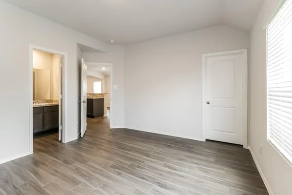 an empty room with wooden floor kitchen view and windows