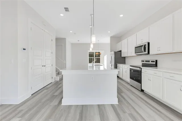 a white kitchen with wooden floor and stainless steel appliances