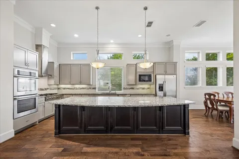 a kitchen with kitchen island granite countertop a stove a sink a refrigerator wooden floor and chairs