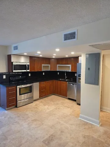 a large kitchen with kitchen island granite countertop a stove top oven a sink a counter space and cabinets