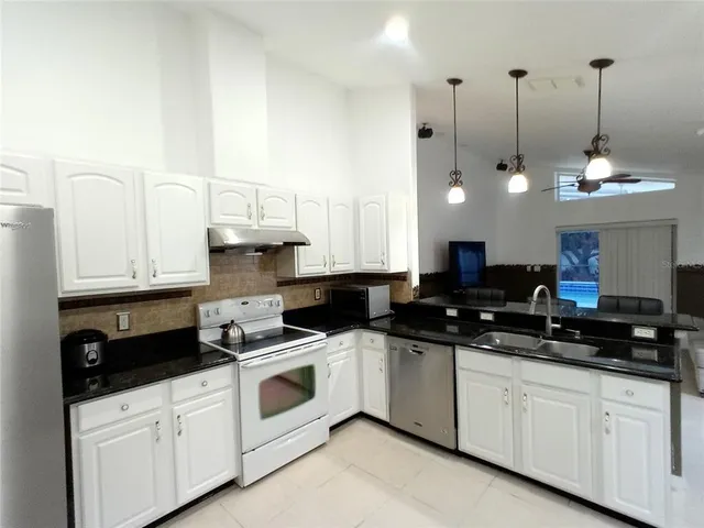a kitchen with stainless steel appliances granite countertop a sink a stove and a white cabinets