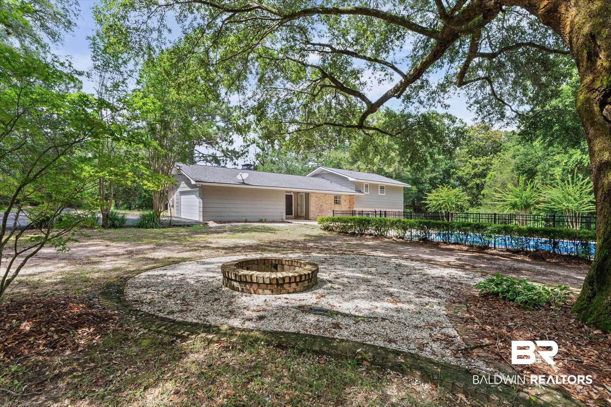 8301 Fordham Road Mobile, AL 36619 - Photo 34 of 57 Expansive backyard featuring a brick fire pit, gravel patio area, mature trees, and a fenced swimming pool