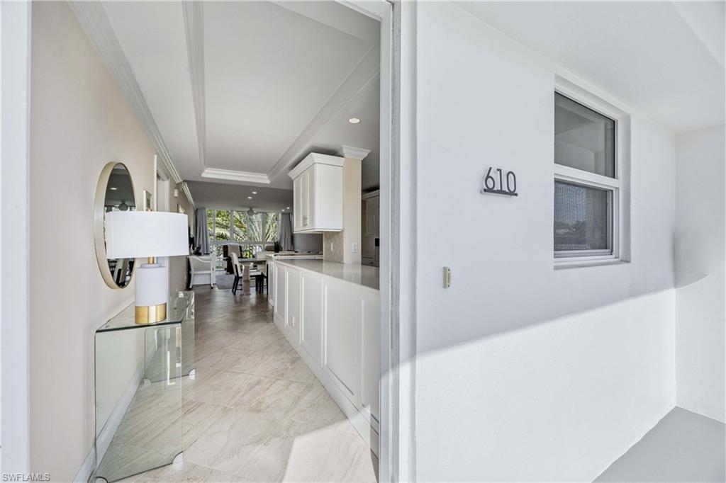 Hallway with recessed lighting, light marble finish floors, a raised ceiling, and ornamental molding