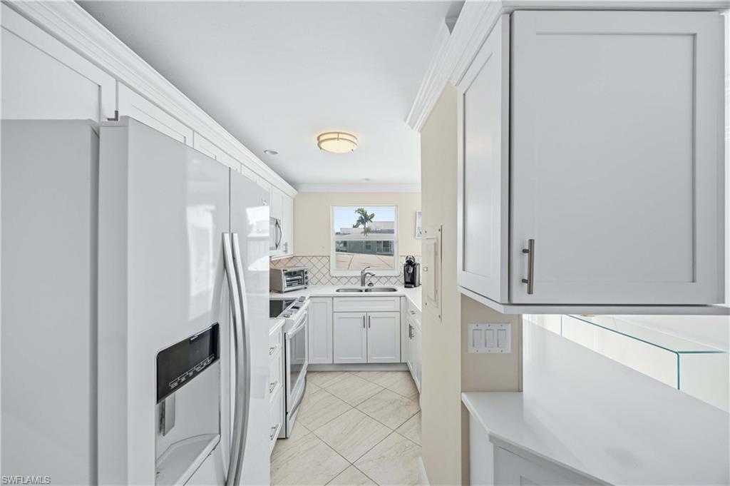 610 Broad Avenue South, Unit J610 Naples, FL 34102 - Photo 4 of 20 Kitchen with white appliances, ornamental molding, tasteful backsplash, white cabinetry, and light tile patterned floors