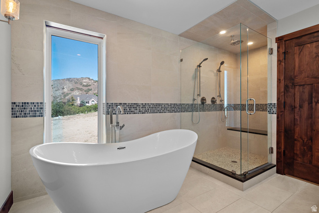 4221 Juniper Circle Alpine, UT 84004 - Photo 15 of 66 Modern bathroom featuring a freestanding soaking tub with floor-mounted faucet, a glass-enclosed shower with dual shower heads and a built-in bench, light-toned tile walls with a mosaic accent band, and a rustic wood door