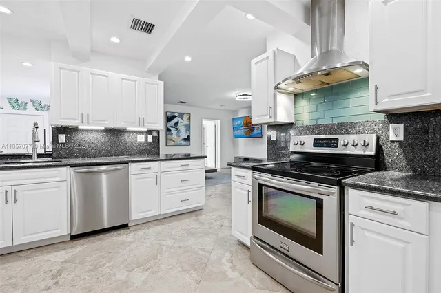 a kitchen with stainless steel appliances granite countertop a stove a sink and white cabinets