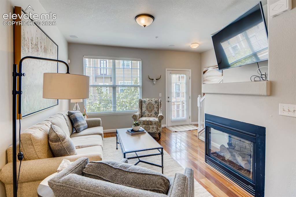 846 Victoria Ridge Point Colorado Springs, CO 80903 - Photo 6 of 27 Living area featuring wood-finish flooring, a built-in fireplace with a mantel, a large window with blinds, and a glass-paneled door