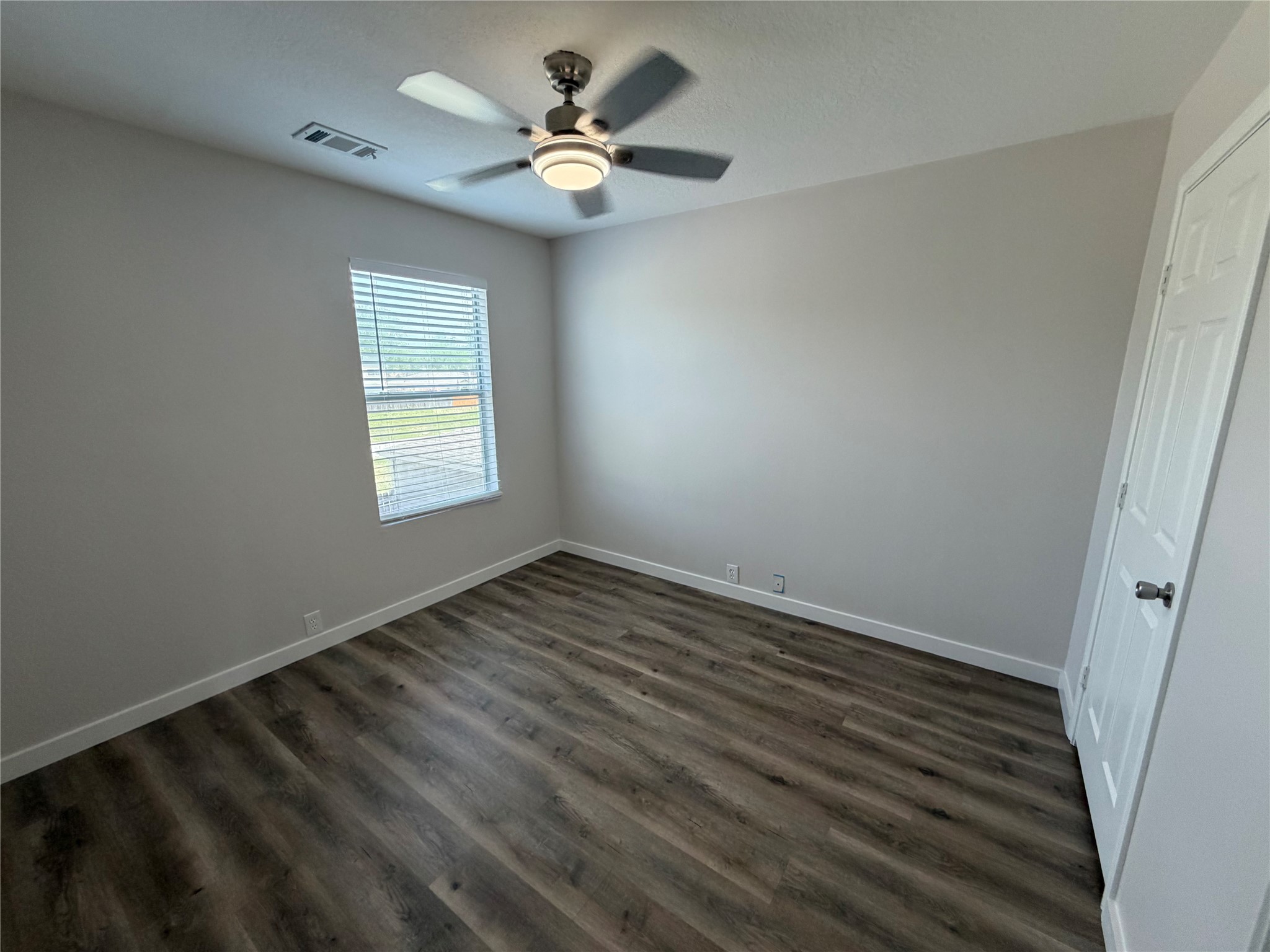 2123 Rustling Trees Way Spring, TX 77373 - Photo 18 of 21 This photo showcases a bright, unfurnished room with light gray walls and wood-look flooring. It features a window with blinds, a ceiling fan, and a white door, offering a clean and modern look.