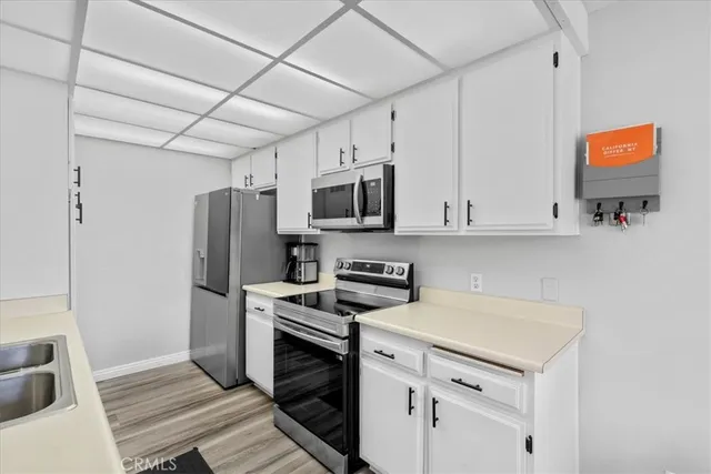 a kitchen with stainless steel appliances granite countertop a sink dishwasher a refrigerator and white cabinets with wooden floor