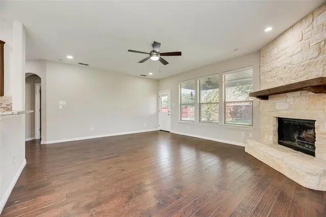 an empty room with windows fireplace and a kitchen view