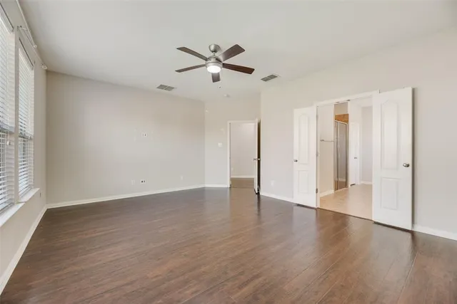 an empty room with wooden floor a ceiling fan and windows