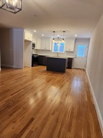 a view of kitchen and empty room with wooden floor