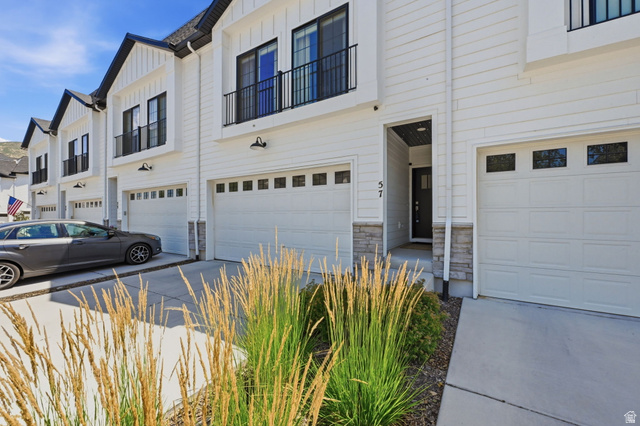 57 McCall Ln. Farmington, UT 84025 - Photo 3 of 36 Contemporary townhome exterior featuring white siding, black trim accents, a double-car garage with transom windows, and a prominent front entry
