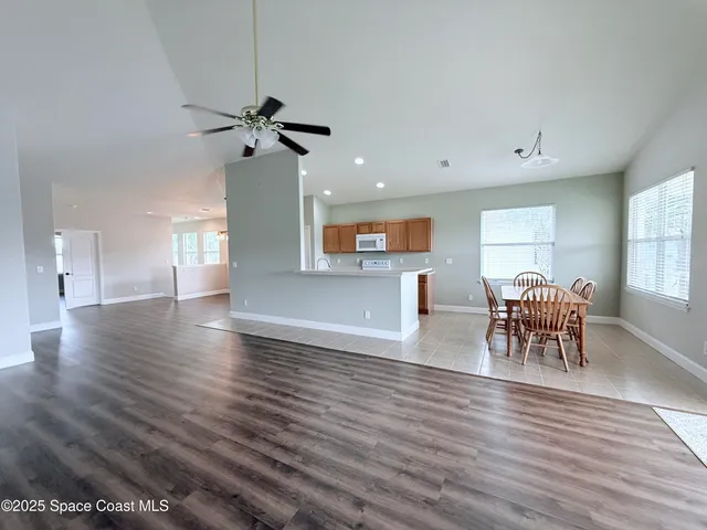 an empty room with wooden floor chandelier fan and windows