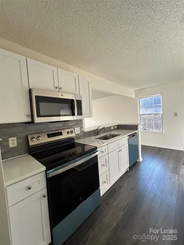 a kitchen with granite countertop a stove top oven a sink dishwasher and white cabinets with wooden floor