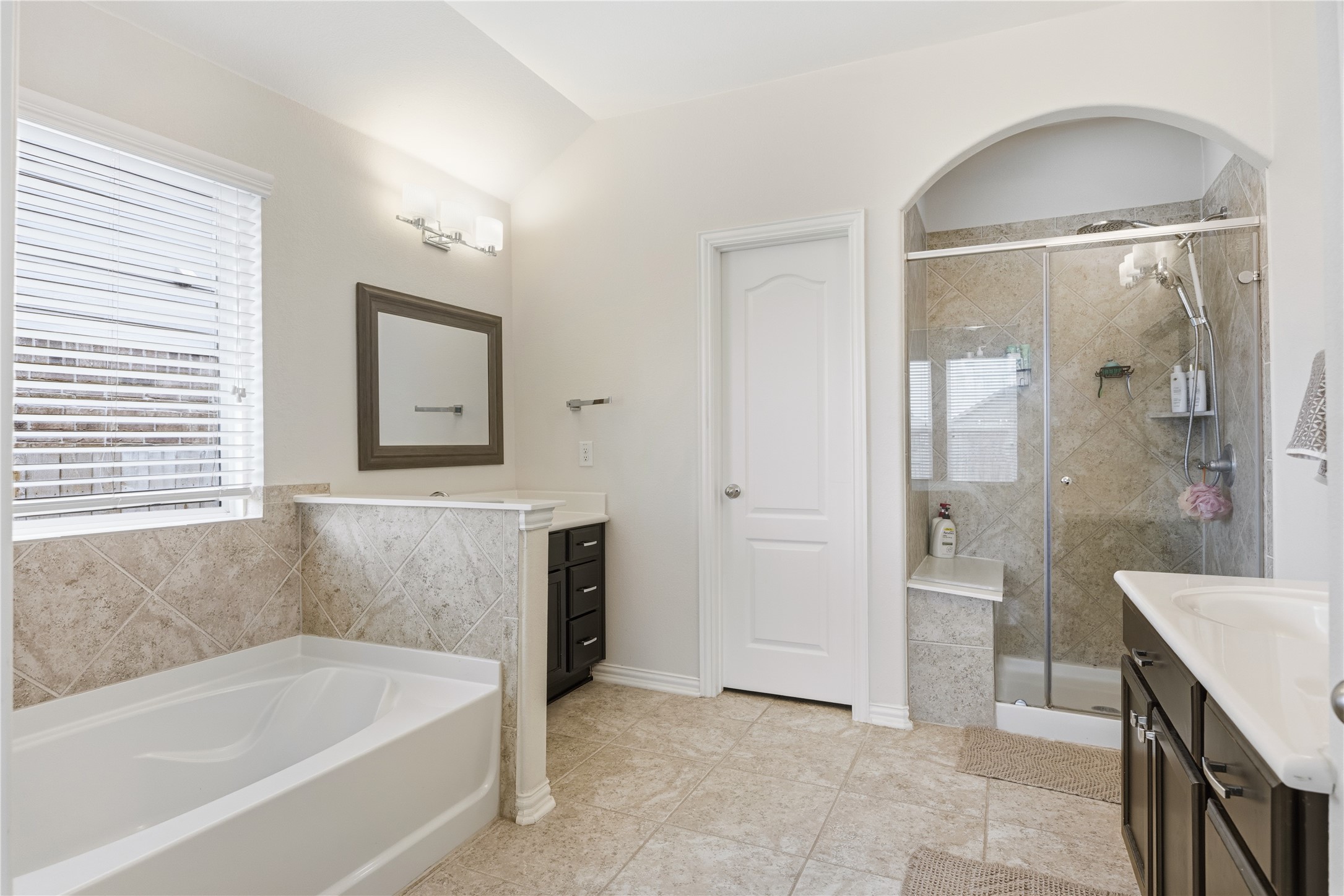 486 Pond View Pass Buda, TX 78610 - Photo 31 of 39 Spacious bathroom featuring a white soaking tub, separate glass-enclosed shower with a built-in bench, dual vanities with dark cabinetry, and neutral tile flooring