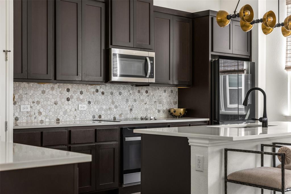 7537 Laburnam Road Dallas, TX 75228 - Photo 9 of 30 Dark wood-finish cabinetry, patterned tile backsplash, white countertops, built-in stainless steel microwave, and a black faucet