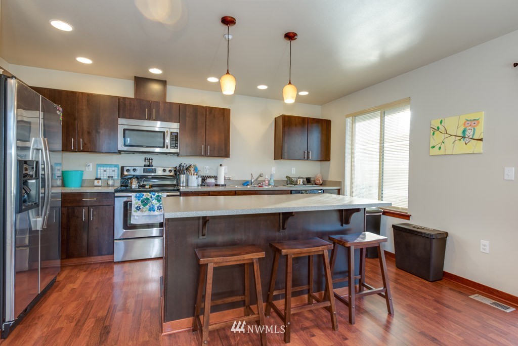 4821 Northeast Sunset Boulevard Renton, WA 98059 - Photo 7 of 12 a kitchen with stainless steel appliances granite countertop a refrigerator a stove a sink dishwasher a dining table and chairs with wooden floor