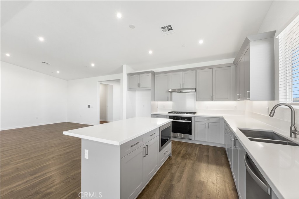 41846 Castello Lane Palmdale, CA 93552 - Photo 18 of 46 a large white kitchen with a stove top oven a sink a refrigerator and white cabinets with wooden floor