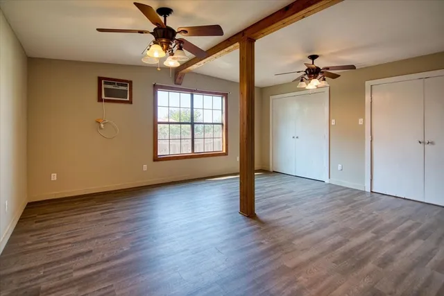 an empty room with wooden floor chandelier fan and windows