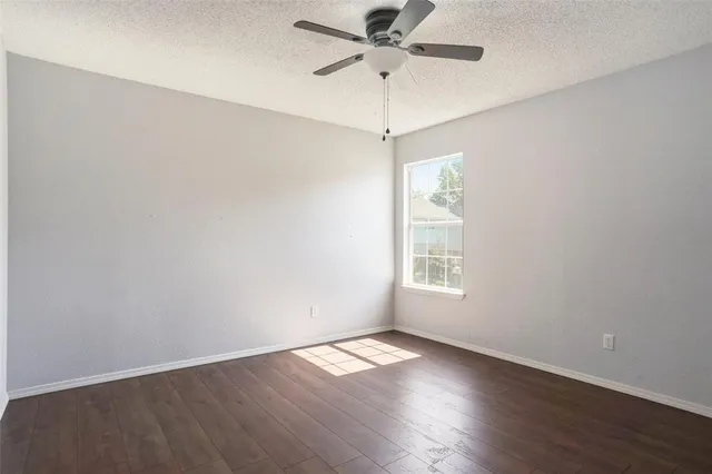 an empty room with wooden floor window and ceiling fan