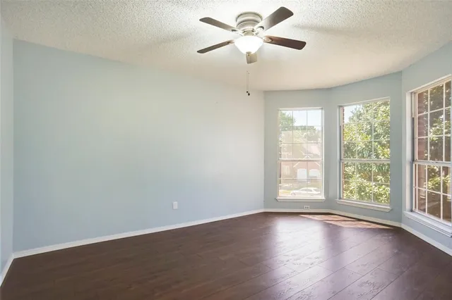 an empty room with wooden floor fan and windows
