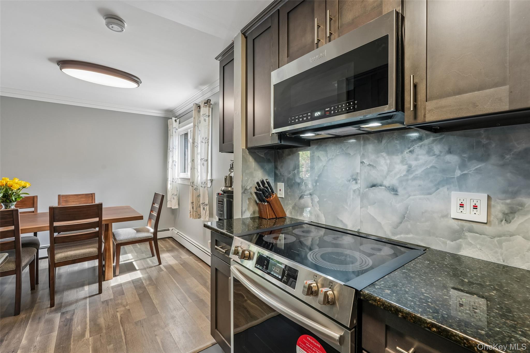2 Secora Road, Unit C5 Monsey, NY 10952 - Photo 16 of 32 Stainless steel electric range, dark granite-style countertop, full-height backsplash, wood-finish flooring, and dark wood-finish cabinetry