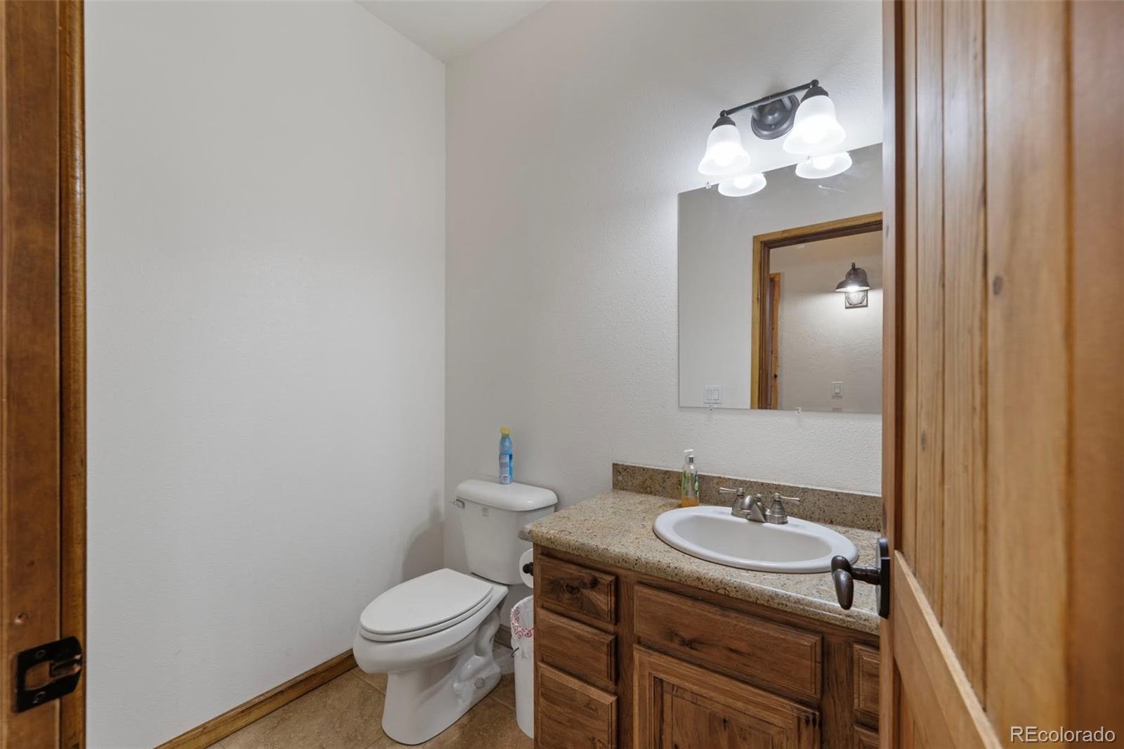 988 P Street Penrose, CO 81240 - Photo 16 of 48 a bathroom with a granite countertop toilet a sink and mirror
