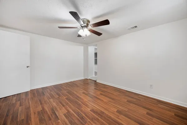 an empty room with wooden floor fan and windows