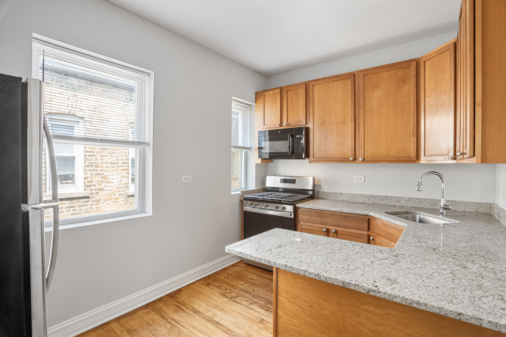 7326 North Damen Avenue, Unit 3 Chicago, IL 60645 - Photo 4 of 14 a kitchen with stainless steel appliances granite countertop wooden cabinets a stove a sink and dishwasher with wooden floor