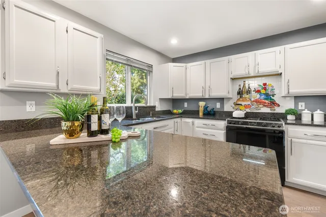 a kitchen with kitchen island granite countertop a stove a sink cabinets and living room view