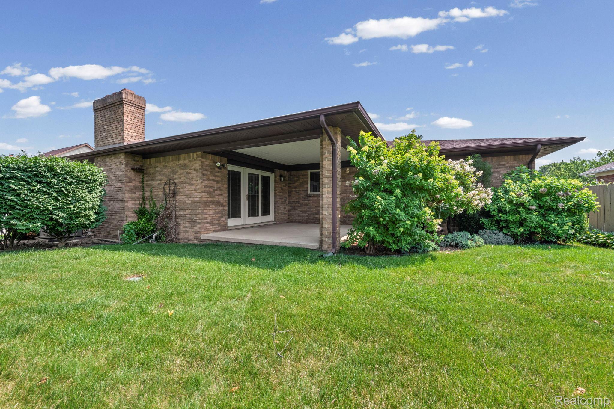 21580 Georgetown Road Trenton, MI 48183 - Photo 33 of 36 Expansive lawn featuring mature landscaping, a covered patio, brick exterior, and a prominent brick chimney