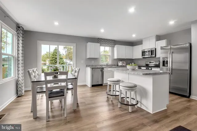 a kitchen with stainless steel appliances granite countertop a refrigerator a stove top oven a sink dishwasher and white cabinets with wooden floor