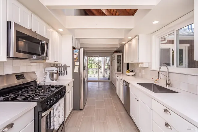 a kitchen with stainless steel appliances a sink dishwasher a stove top oven a refrigerator with white cabinets and wooden floor