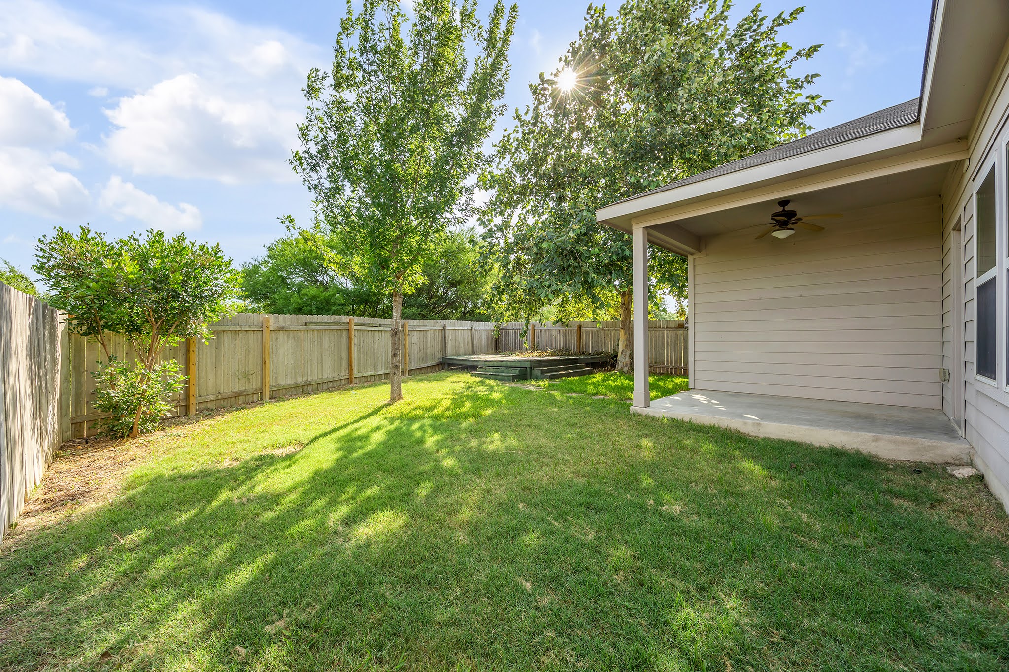 7212 Vail Ridge Street Austin, TX 78744 - Photo 20 of 26 A fenced backyard offers a shaded concrete patio and a raised wooden deck perfect for outdoor enjoyment.